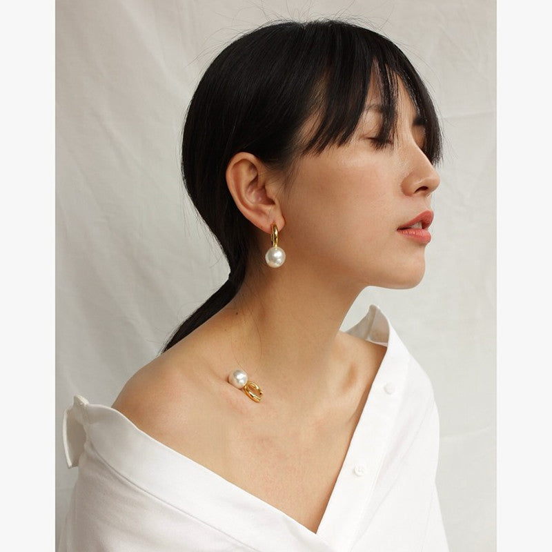 Gold-tone huggie earring with a small white pearl-style drop, worn with a white blouse