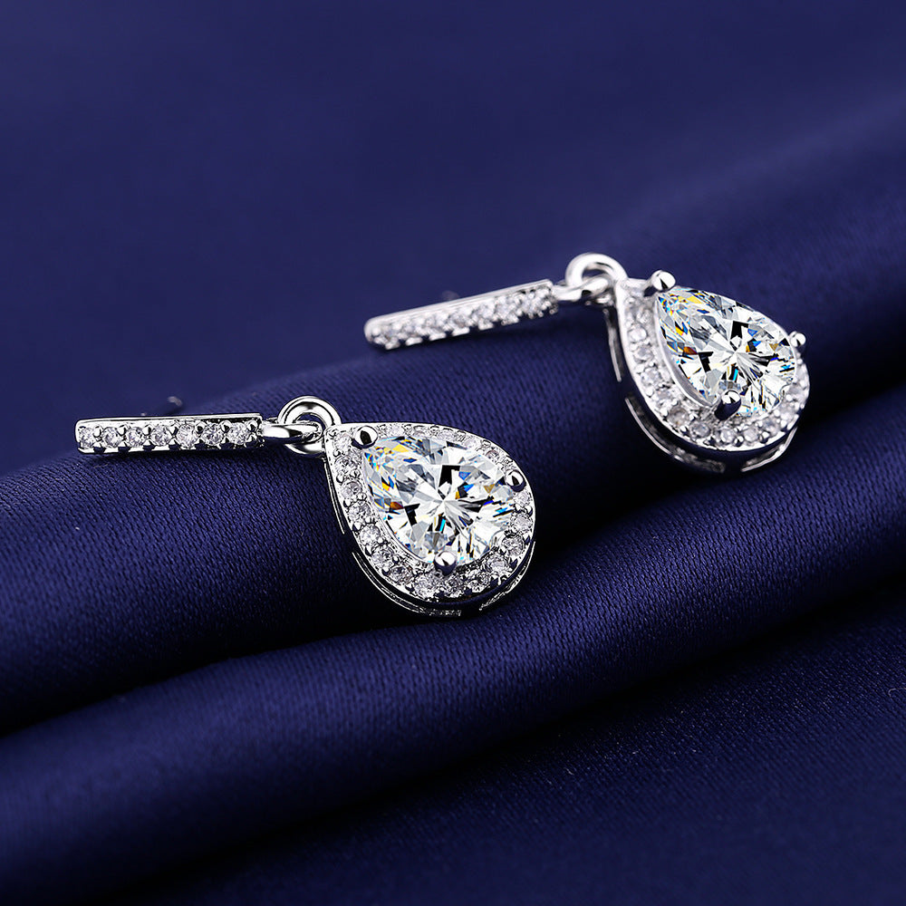 Silver-tone halo zircon teardrop earrings on deep blue satin, side angle