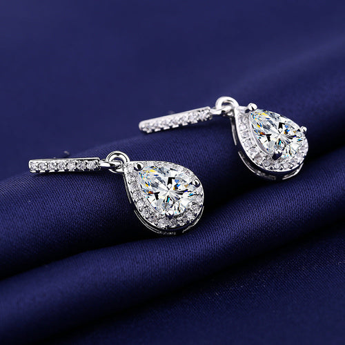 Silver-tone halo zircon teardrop earrings on deep blue satin, side angle
