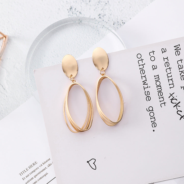 Gold-tone layered open-oval drop earrings with matte oval disc tops, laid flat on a white card