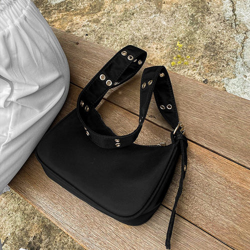 Black shoulder bag with a gold-tone eyelet strap and buckle resting on a wooden bench