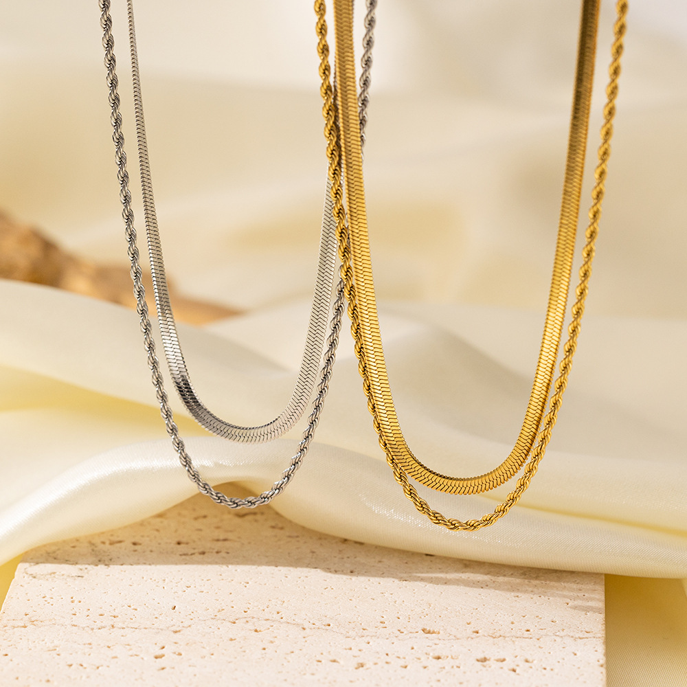 Silver-tone and gold-tone double-layer herringbone and rope chain necklaces draped over cream satin