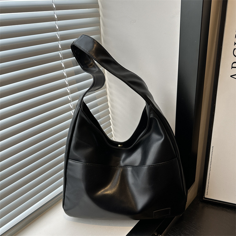 Black slouchy shoulder bag with a wide single strap and front seam, shown by a window with blinds