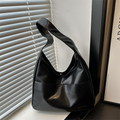 Black slouchy shoulder bag with a wide single strap and front seam, shown by a window with blinds