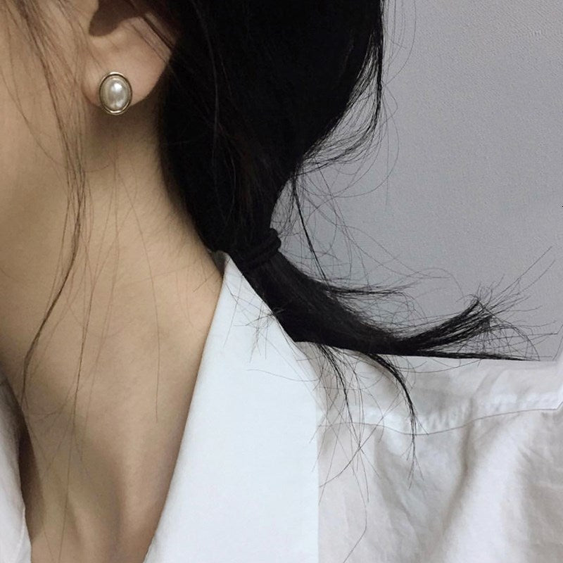 Oval pearl-style stud earring with gold-tone rim, worn