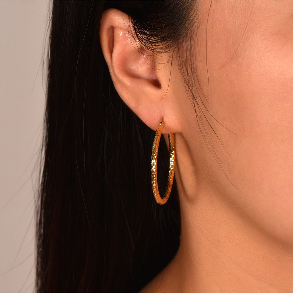 Gold-tone textured hoop earring worn on the ear