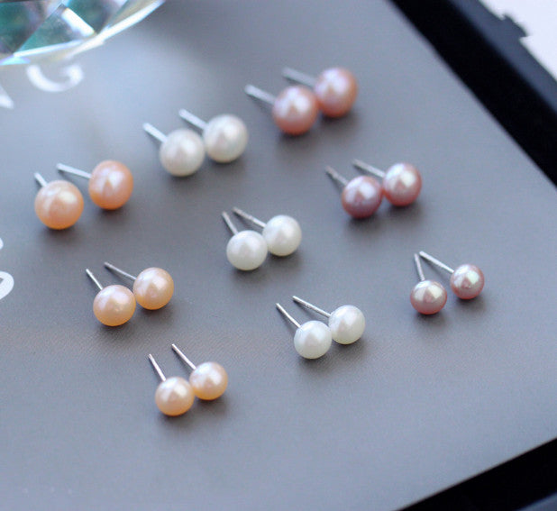 Pearl-style stud earrings in several colors on a grey tray