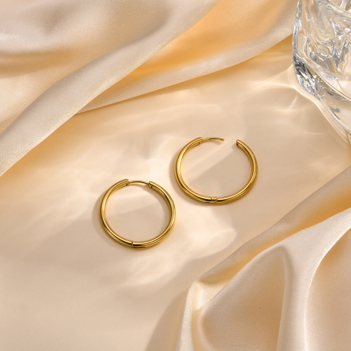 Pair of gold-tone huggie hoop earrings on cream satin