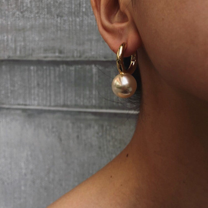 Gold-tone huggie hoop earring with champagne pearl-style drop, worn