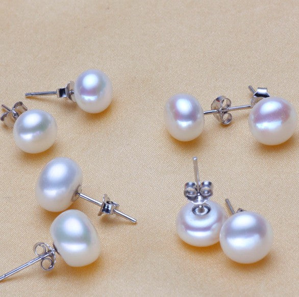 White pearl-style stud earrings with silver-tone posts on a beige surface