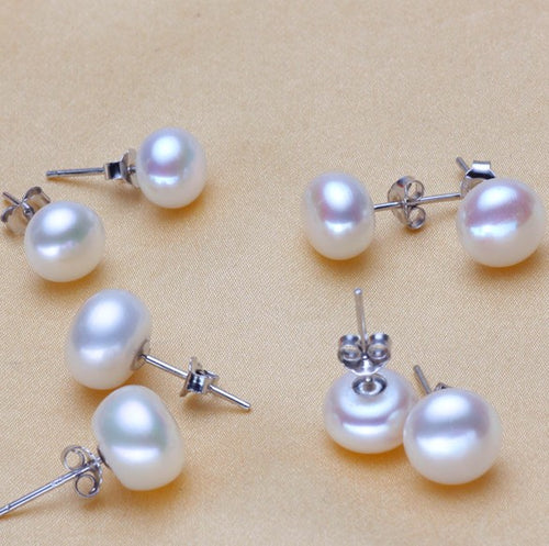 White pearl-style stud earrings with silver-tone posts on a beige surface