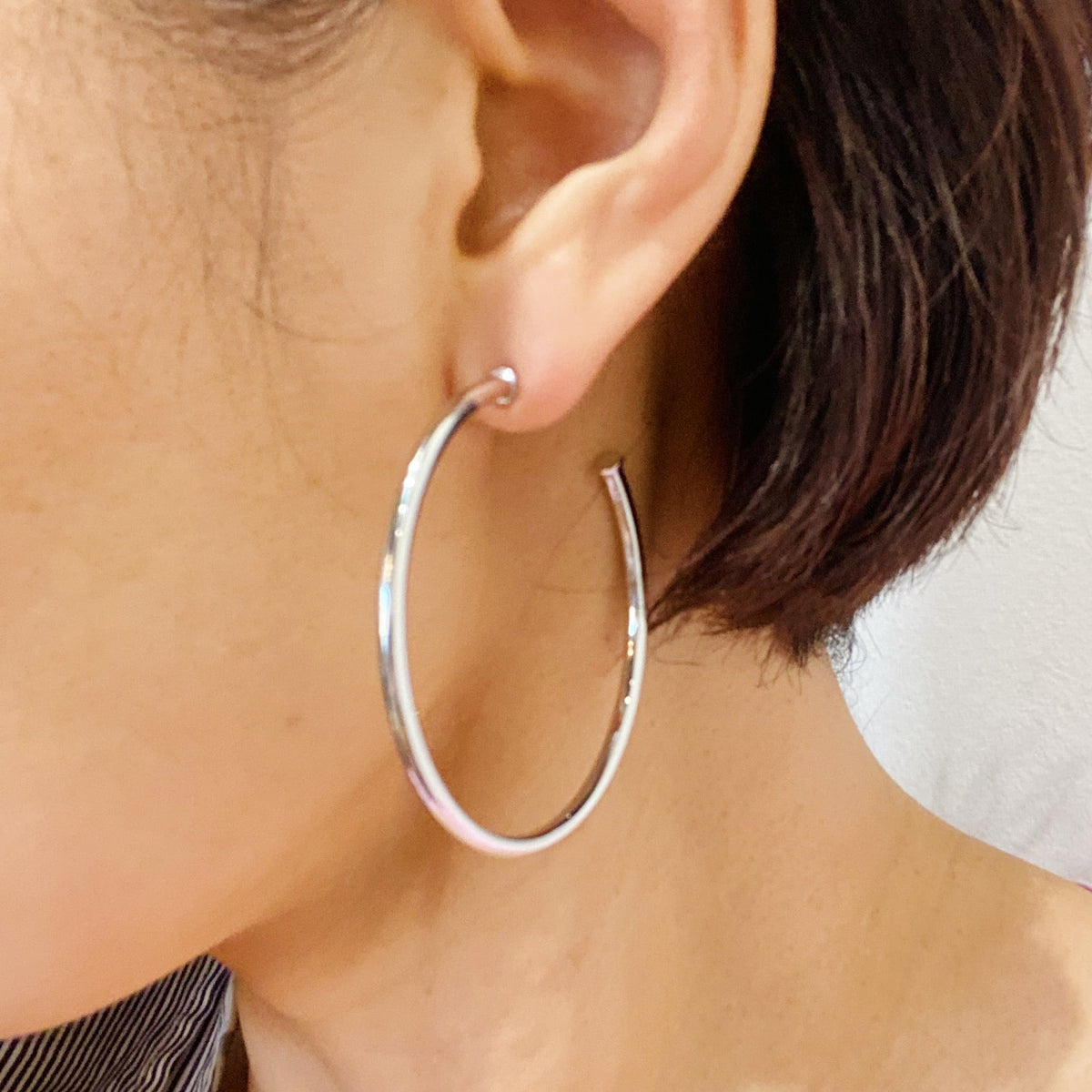 Thin silver-tone hoop earring worn on the ear, hanging to about the jawline