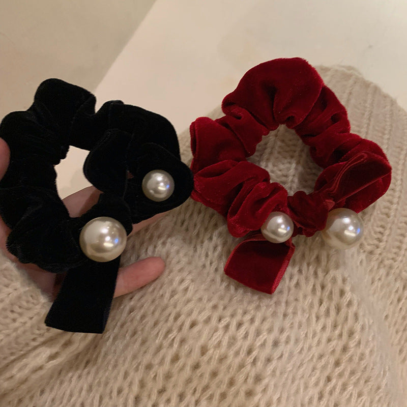 Black and wine red bow scrunchies with pearl-style beads against a cream knit sweater