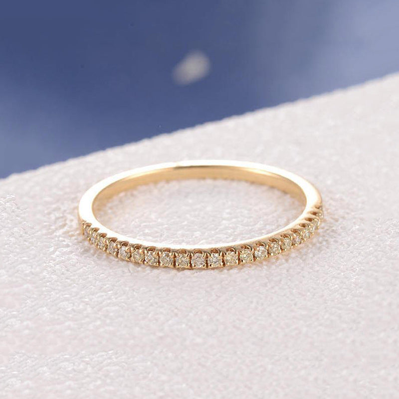 Gold-tone stacking band with a row of small zircon stones on a white textured surface