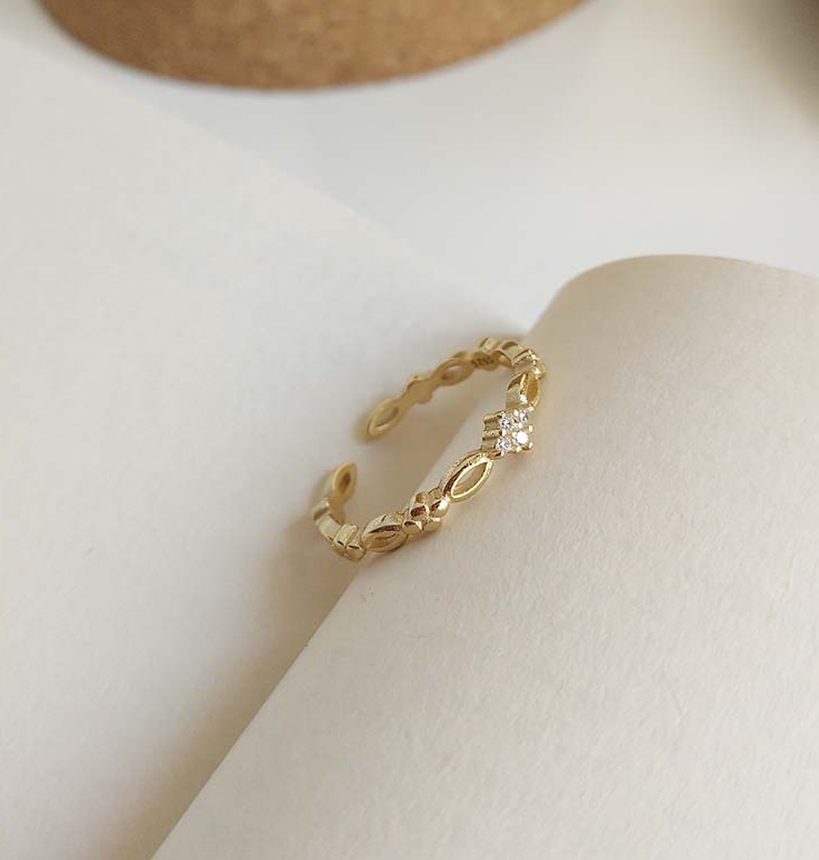 Gold-tone open ring with link band and zircon-style stone, angled view on an open book