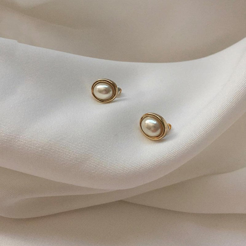 Pair of oval pearl-style stud earrings with gold-tone rims on white satin