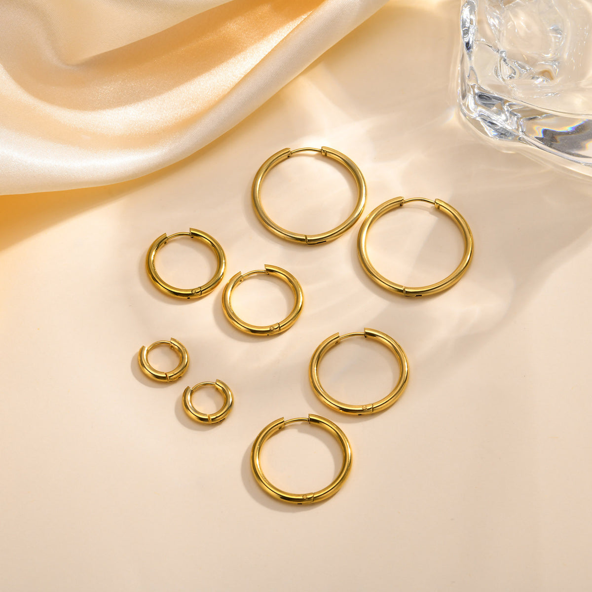 Gold-tone huggie hoop earrings in four graduated sizes on cream satin