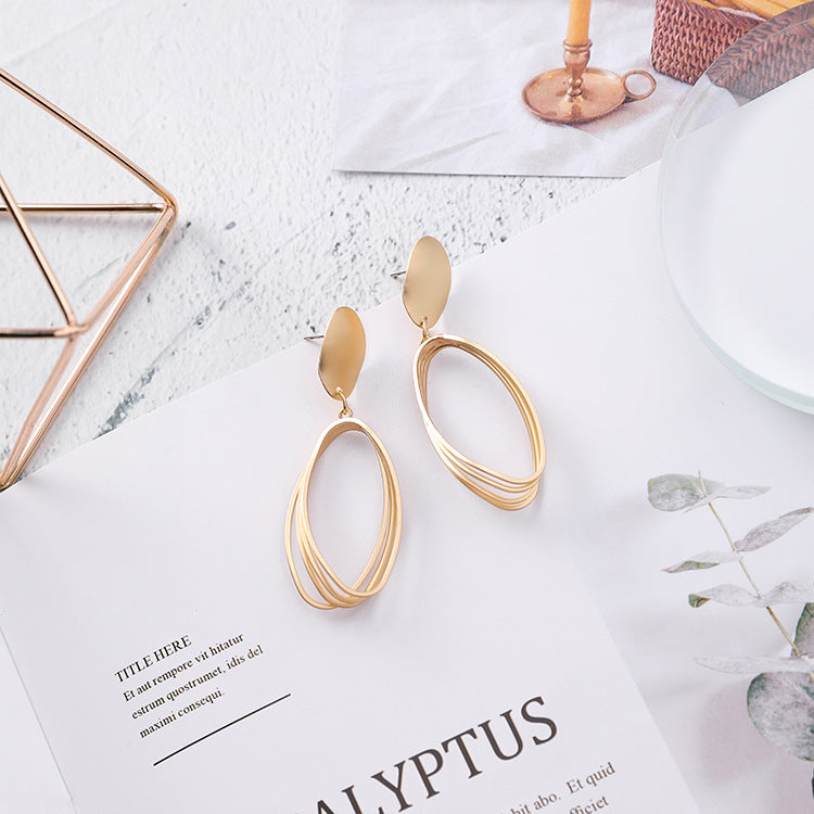 Gold-tone layered open-oval drop earrings with matte oval disc tops, angled to show the stud posts