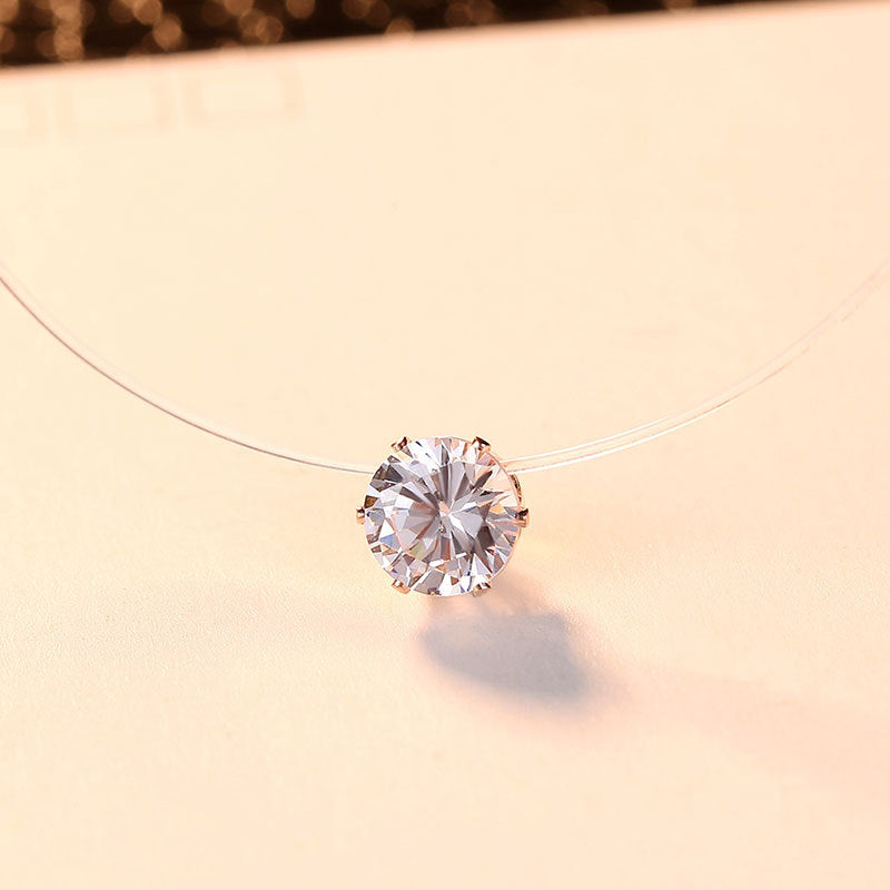 Zircon pendant floating on a clear cord, rose gold-tone setting, warm beige background