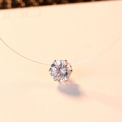 Zircon pendant floating on a clear cord, rose gold-tone setting, warm beige background