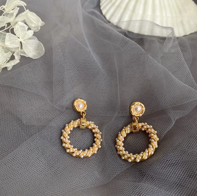 Pair of twisted gold-tone ring drop earrings with a pearl-style top on grey tulle