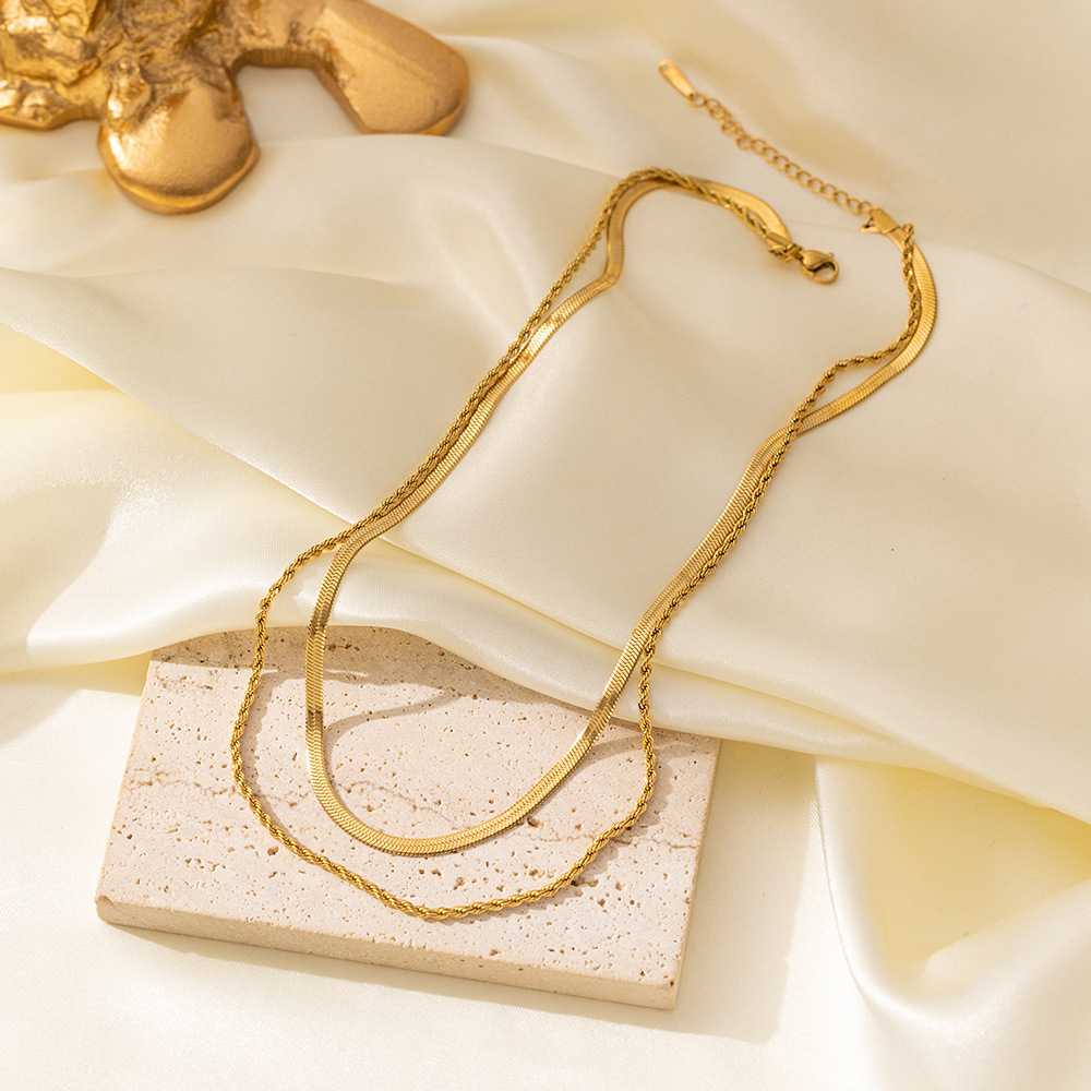 Gold-tone herringbone and rope chain necklace laid on cream satin and a stone block