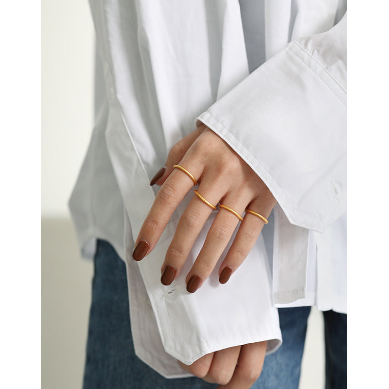 Gold-tone textured stacking rings worn one per finger, white shirt cuff and denim