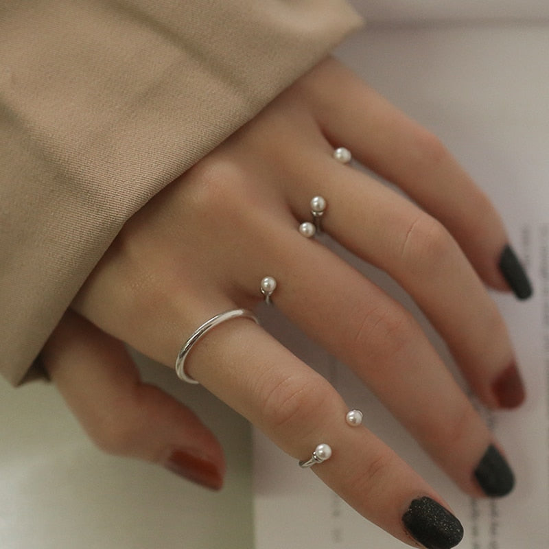 Silver-tone open rings with pearl-style bead ends worn on several fingers, beige sleeve