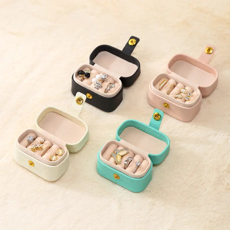 Four open mini ring travel cases in black, pink, cream and aqua, each holding rings