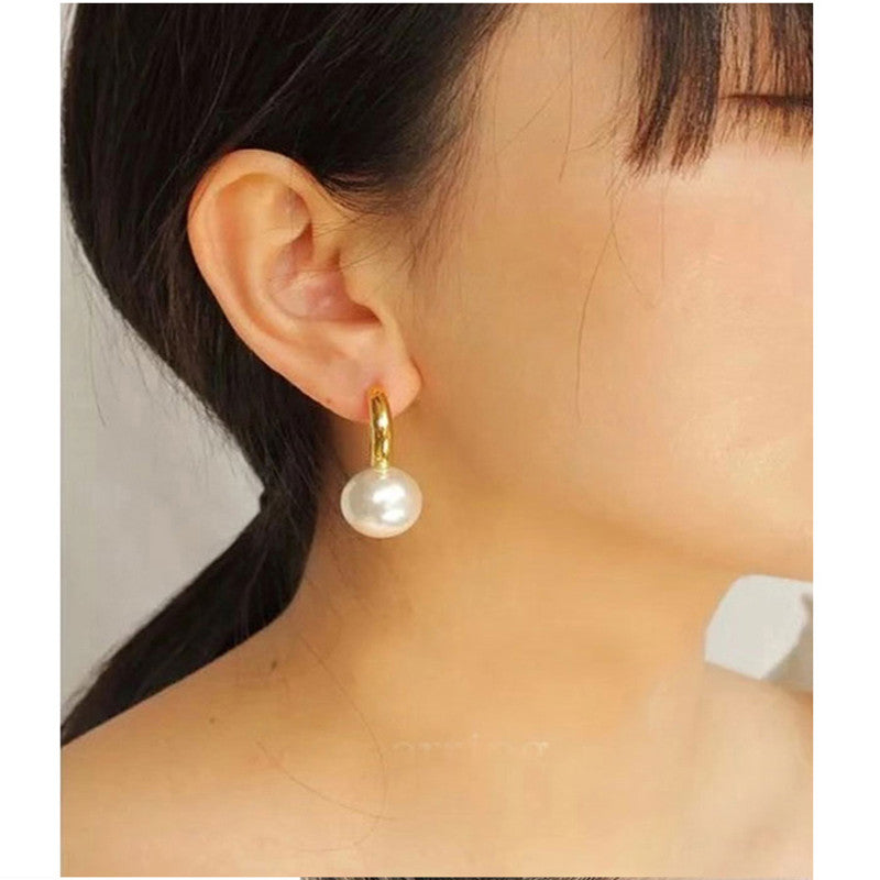 Gold-tone huggie hoop earring with white pearl-style drop, worn, side view