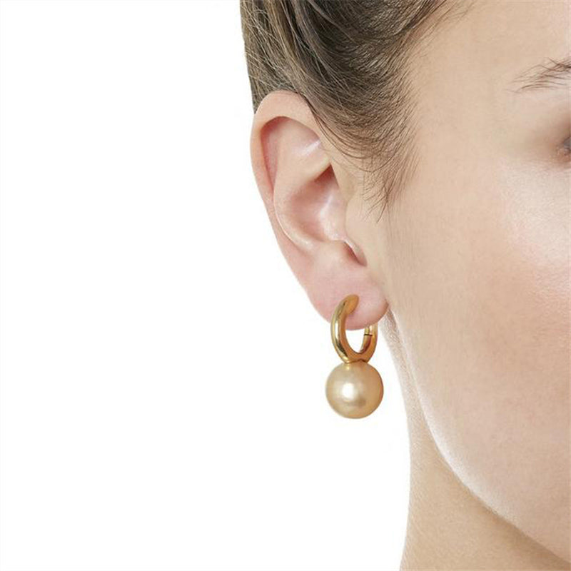 Gold-tone huggie hoop earring with champagne pearl-style drop, worn, close view