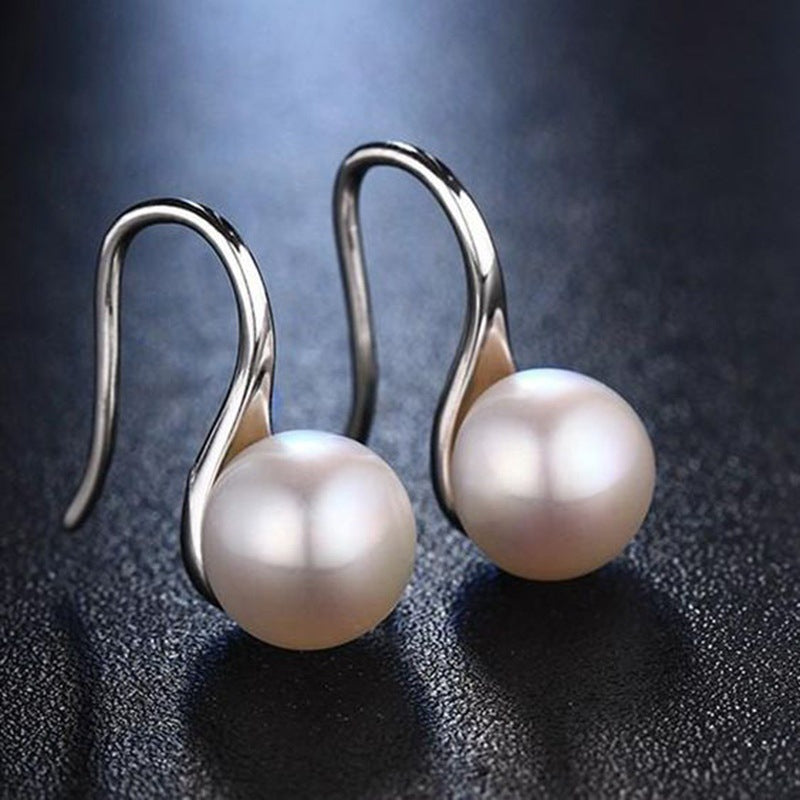 Silver-tone hook drop earrings with round pearl-style beads on a dark textured surface