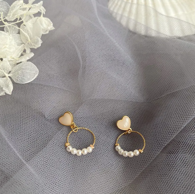 Pair of gold-tone hoop drop earrings with pearl-style beads and a heart-shaped top on grey tulle