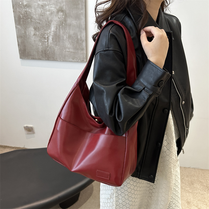 Woman in a black jacket carrying the wine red slouchy shoulder bag on her shoulder