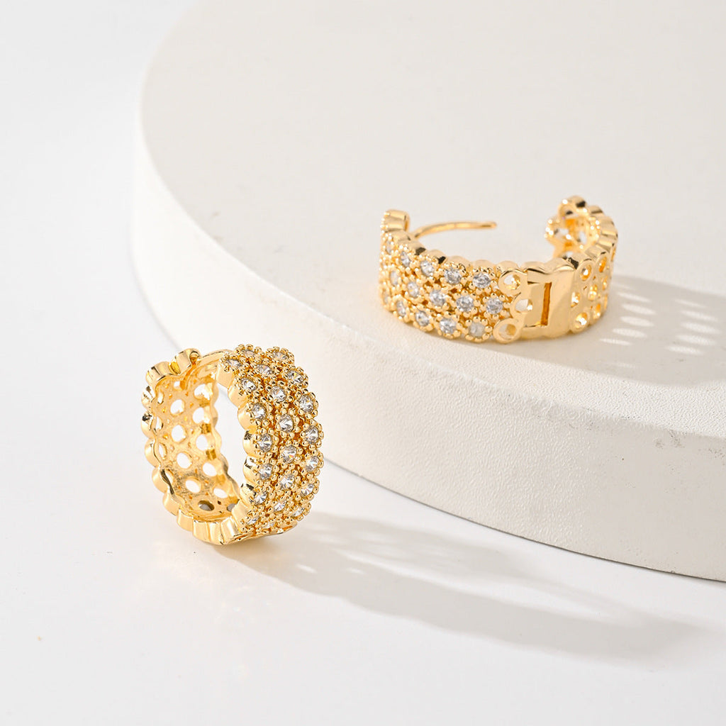 Gold-tone pave zircon huggie hoops, one open to show the hinged post, on and beside a white stand