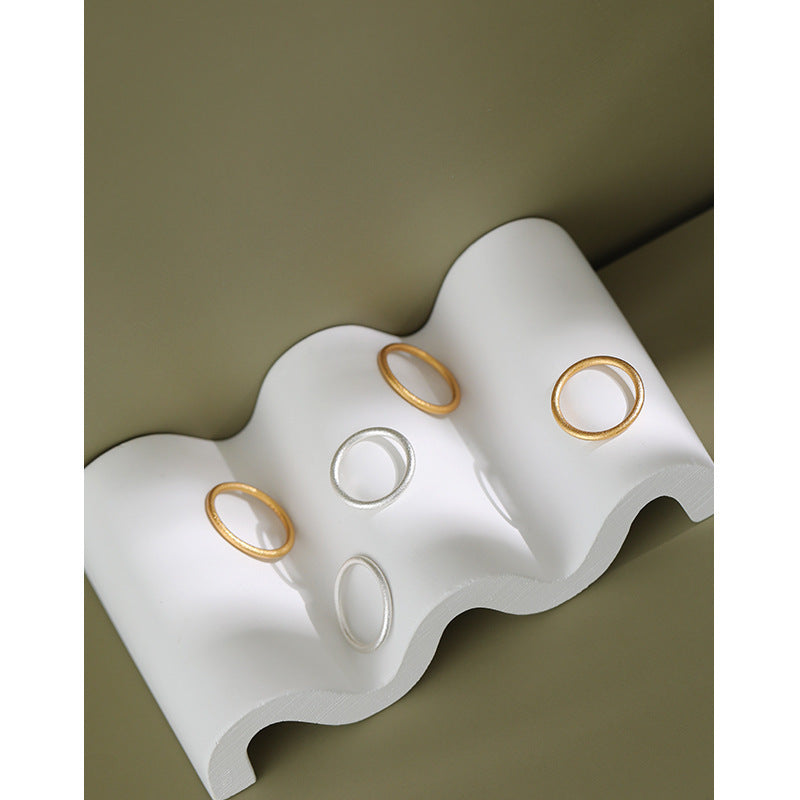 Gold-tone and silver-tone textured stacking rings displayed on a white wave-shaped stand