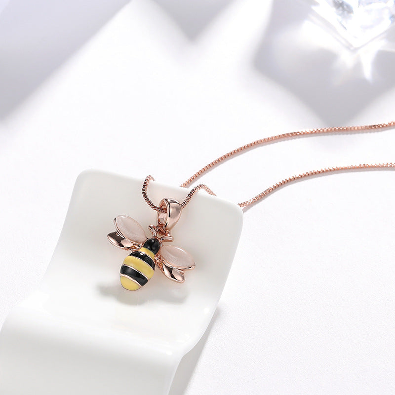 Rose gold-tone bee pendant necklace resting on a white ceramic block