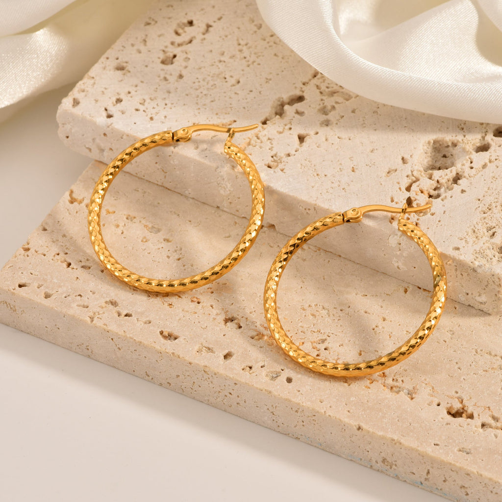 Gold-tone hoop earrings with a criss-cross textured pattern on a stone block with cream satin