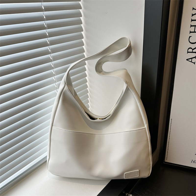 Cream slouchy shoulder bag with a wide single strap and front seam, shown by a window with blinds