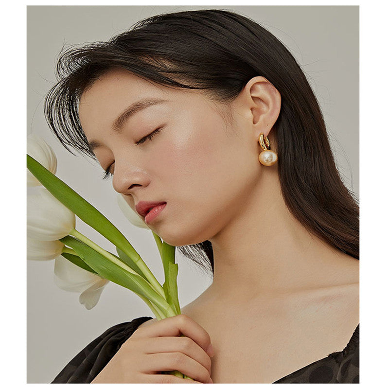 Gold-tone huggie hoop earring with white pearl-style drop, worn with white tulips