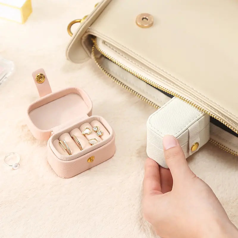 Cream mini ring case slipped into a handbag beside an open pink case with rings