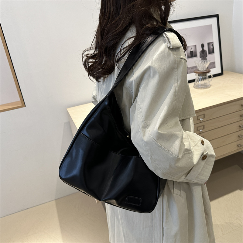 Woman in a light coat carrying the black slouchy shoulder bag on her shoulder