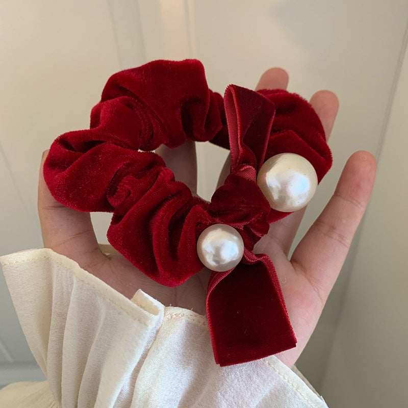 Wine red velvet-look bow scrunchie with pearl-style beads held in an open hand
