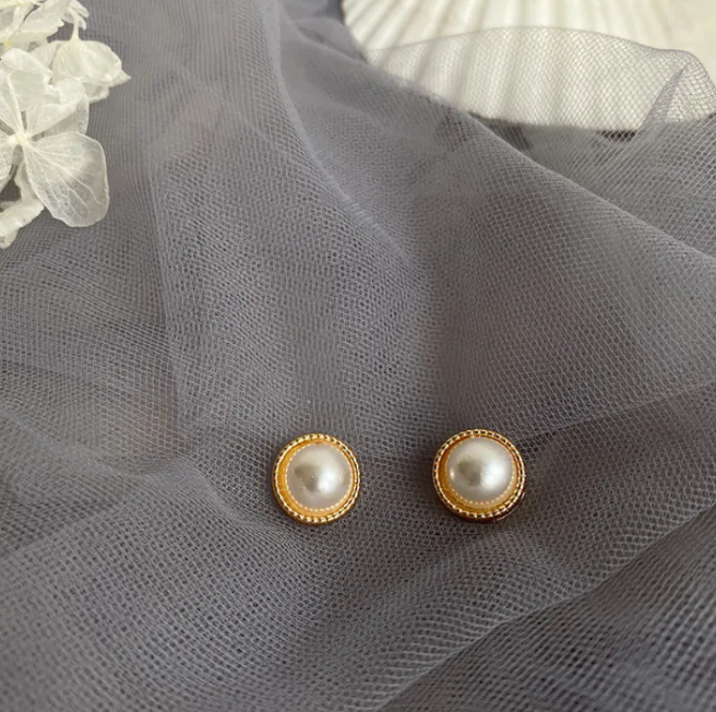 Round pearl-style button earrings with a gold-tone rim on grey tulle