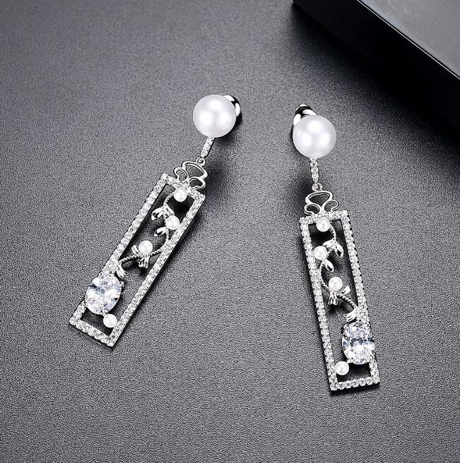 Pair of silver-tone drop earrings with zircon-style stones and vine detail on a dark surface