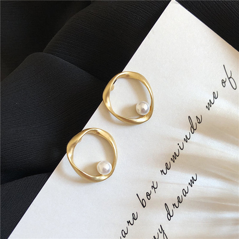 Gold-tone open circle earrings with a pearl-style bead on black fabric and a printed card
