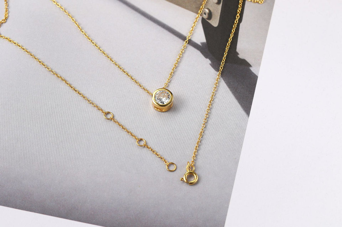 Gold-tone bezel zircon pendant necklace with extender chain on a grey card
