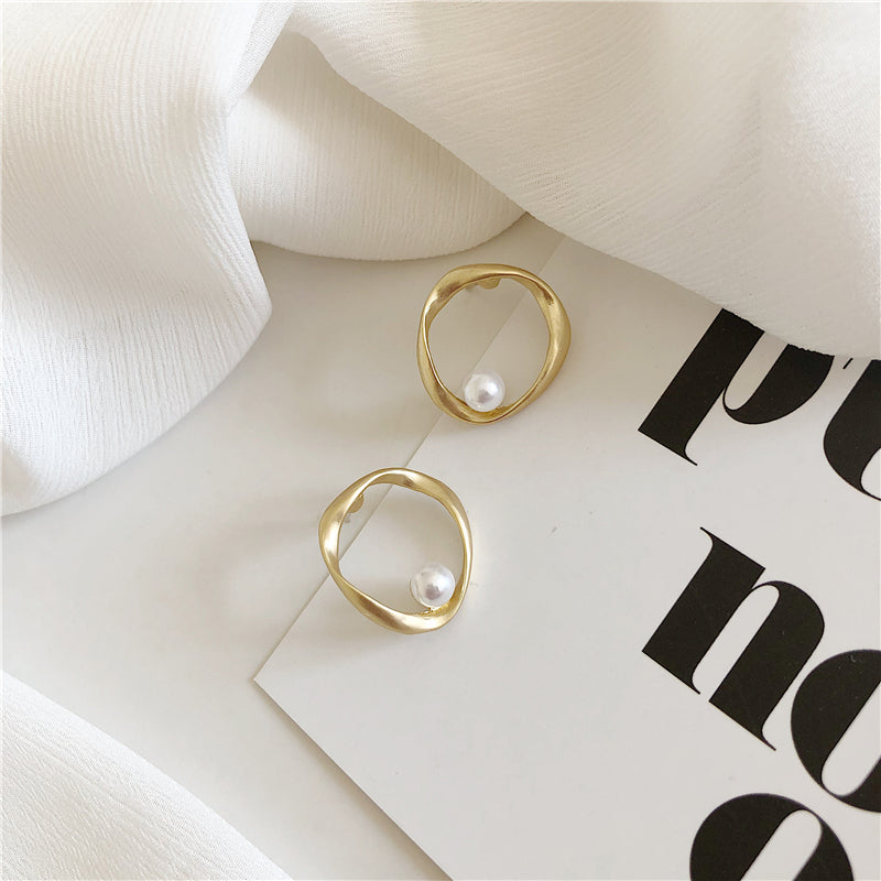 Pair of gold-tone open circle earrings with a pearl-style accent on white fabric and a printed card