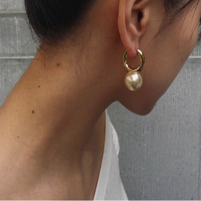 Gold-tone huggie hoop earring with champagne pearl-style drop, worn, side view
