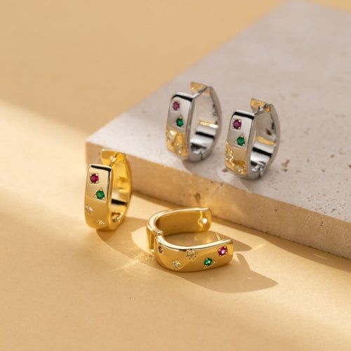 Gold-tone and silver-tone huggie hoops with tiny pink, green and clear zircon accents on a stone block
